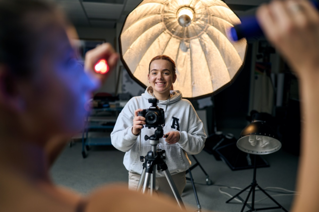 Student smiling as she takes a photograph in the photography studio
